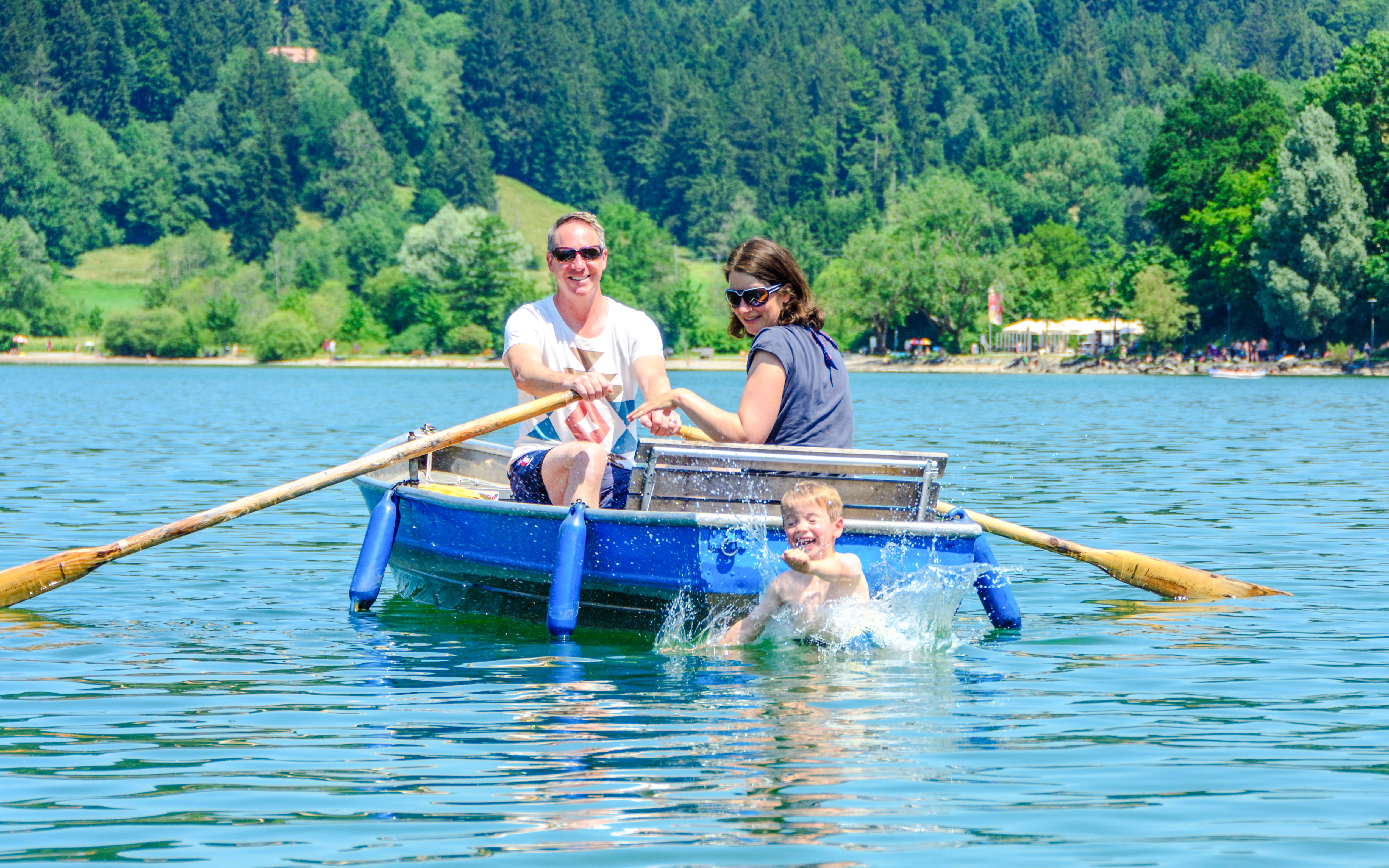Rowboat on Alpsee Lake with family enjoying the water and scenic forest backdrop.