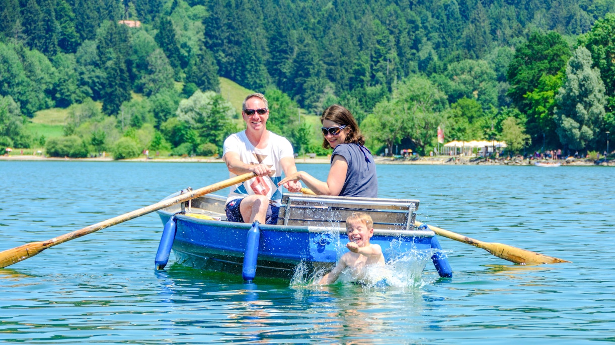 Rowboat on Alpsee Lake with family enjoying the water and scenic forest backdrop.