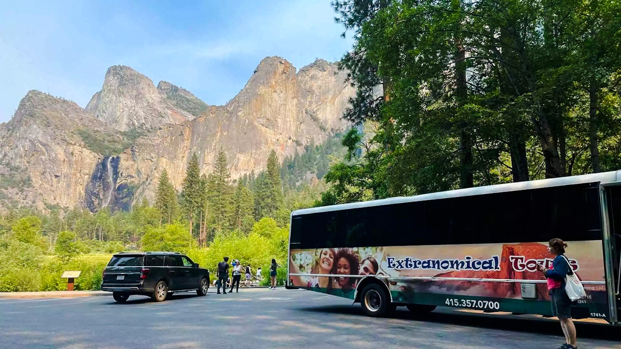 Tour bus and visitors at Yosemite National Park with mountain backdrop, California.