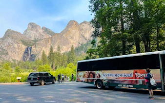 Tour bus and visitors at Yosemite National Park with mountain backdrop, California.