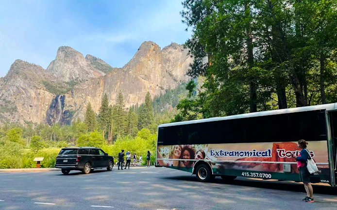 Tour bus and visitors at Yosemite National Park with mountain backdrop, California.