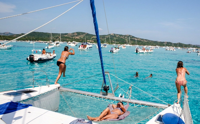 Catamaran tour in La Maddalena Archipelago with people swimming and relaxing on deck.