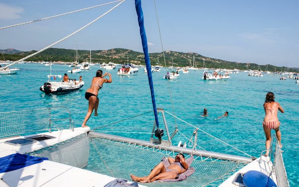 Catamaran tour in La Maddalena Archipelago with people swimming and relaxing on deck.