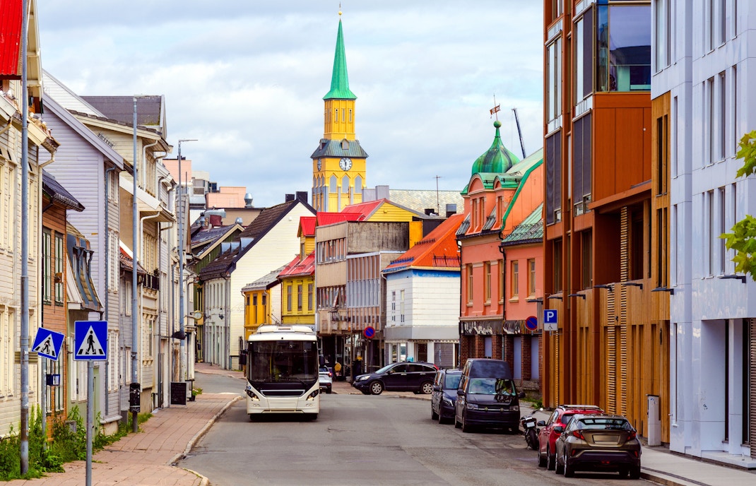 Street view of Tromsø's Storgata with colorful buildings and a church tower in the background.