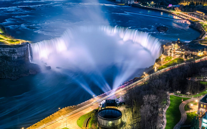 Niagara Falls illuminated at night, view from Canadian side with city lights.