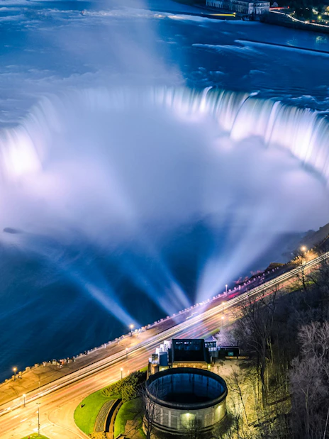 Niagara Falls illuminated at night, view from Canadian side with city lights.