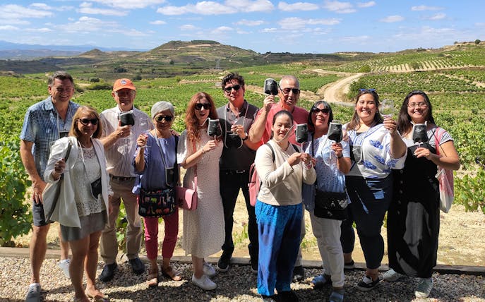 Group enjoying wine tasting at Rioja winery with vineyard backdrop.