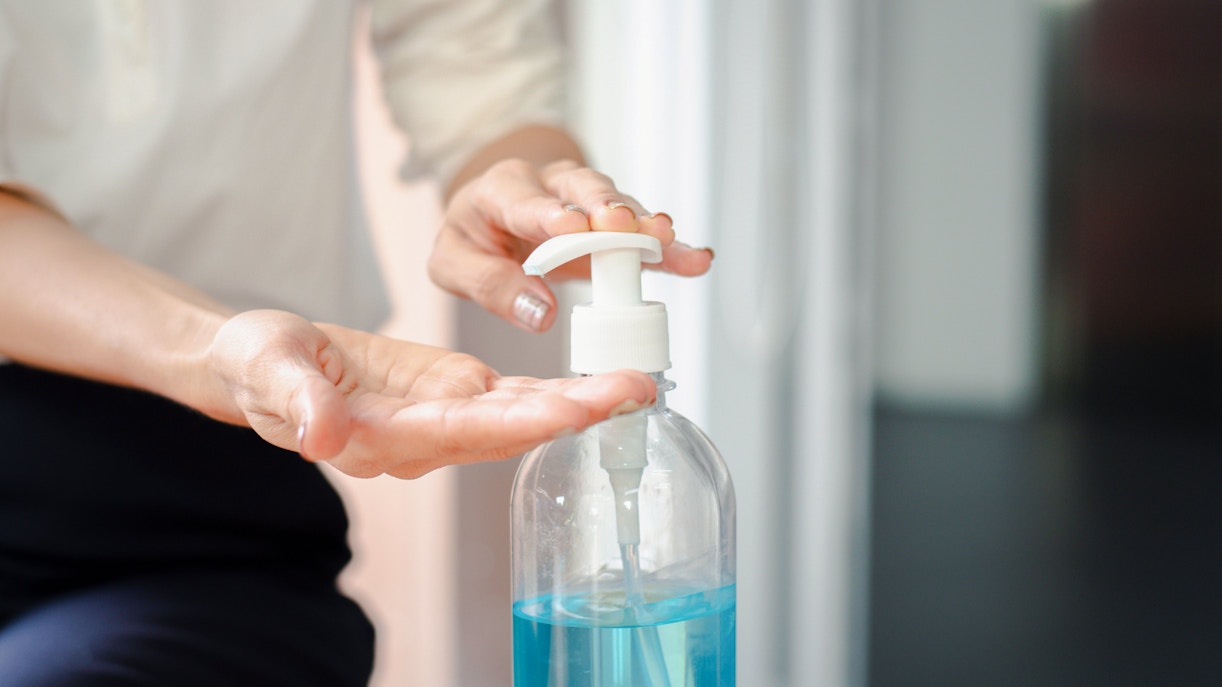 Hand pressing sanitizer pump in a bright room.