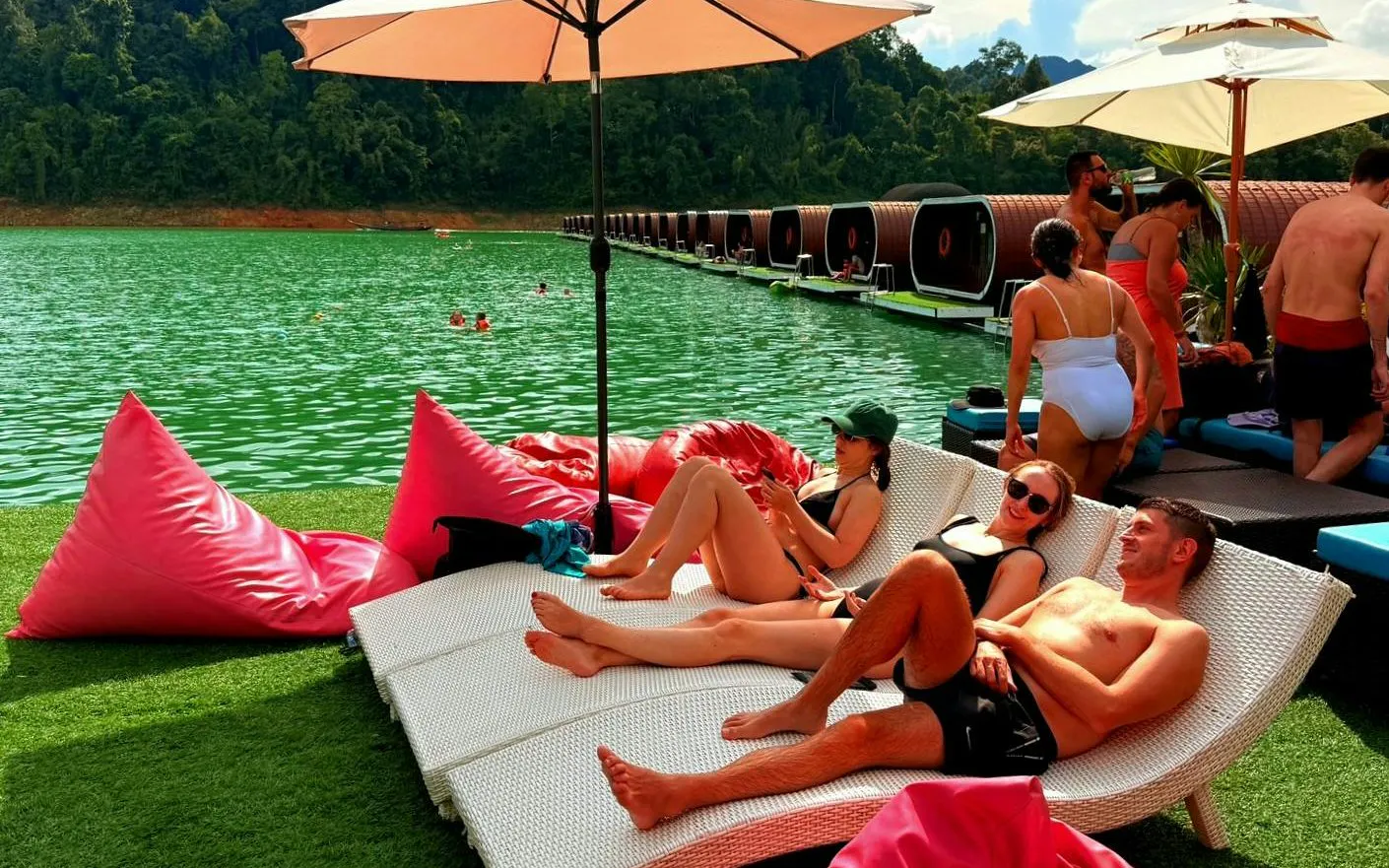 Tourists relaxing on loungers by Cheow Lan Lake, Krabi, with floating bungalows in the background.