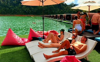 Tourists relaxing on loungers by Cheow Lan Lake, Krabi, with floating bungalows in the background.