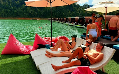 Tourists relaxing on loungers by Cheow Lan Lake, Krabi, with floating bungalows in the background.
