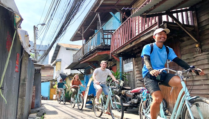 Cyclists ride through a narrow alley on the Bangkok hidden gems bike tour.