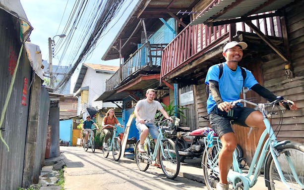 Cyclists ride through a narrow alley on the Bangkok hidden gems bike tour.