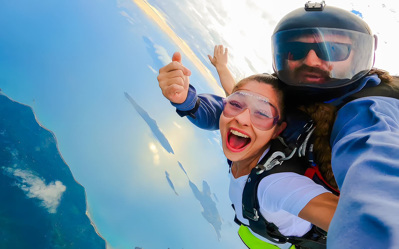 Tandem skydivers over Airlie Beach with ocean and Whitsunday Islands below.