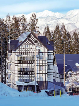Tudor-style lodge at Hakuba47 Mountain Resort with snow-covered trees and mountains.