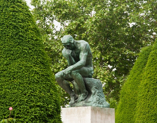 Rodin's The Thinker sculpture in a serene garden setting, Paris, France.