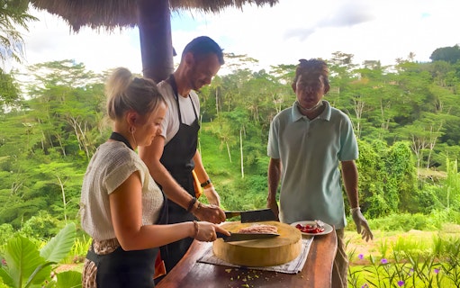 Cooking class participants preparing food with a local instructor in Canggu, overlooking lush countryside.