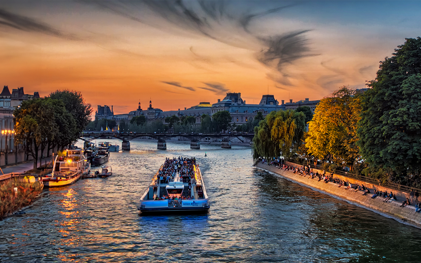 Seine River cruise boat with tourists at sunset near Eiffel Tower, Paris.