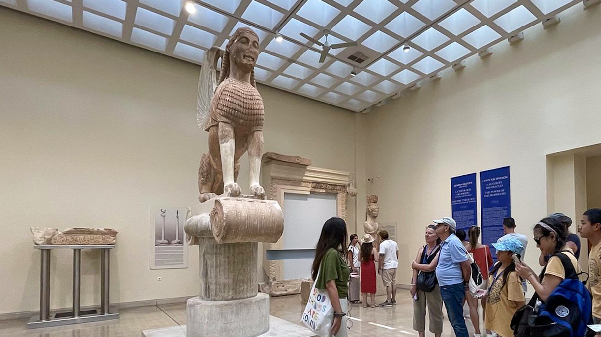 Guide explaining the Sphinx of Naxos to visitors inside Delphi Museum.