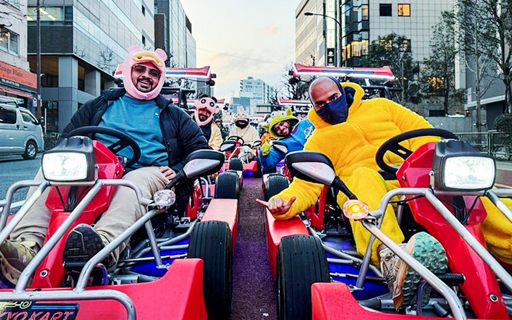 Tourists in costumes driving go-karts on a city street.