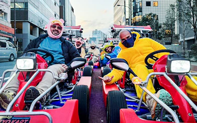 Tourists in costumes driving go-karts on a city street.