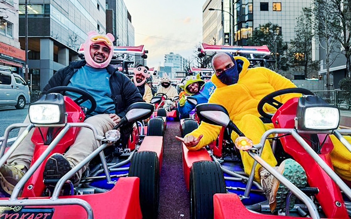 Tourists in costumes driving go-karts on a city street.