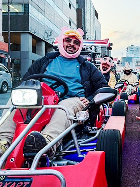 Tourists in costumes driving go-karts on a city street.