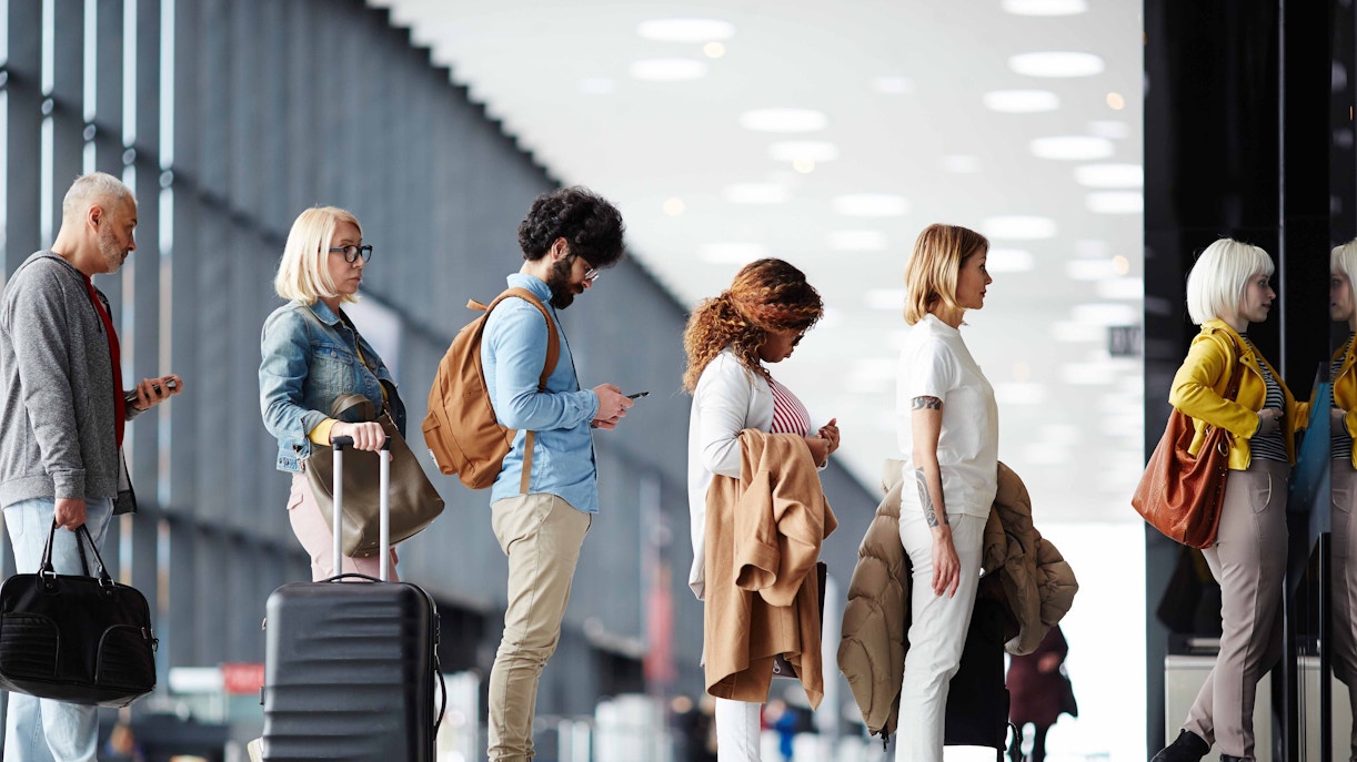 People standing in line at an airport check-in counter with luggage.