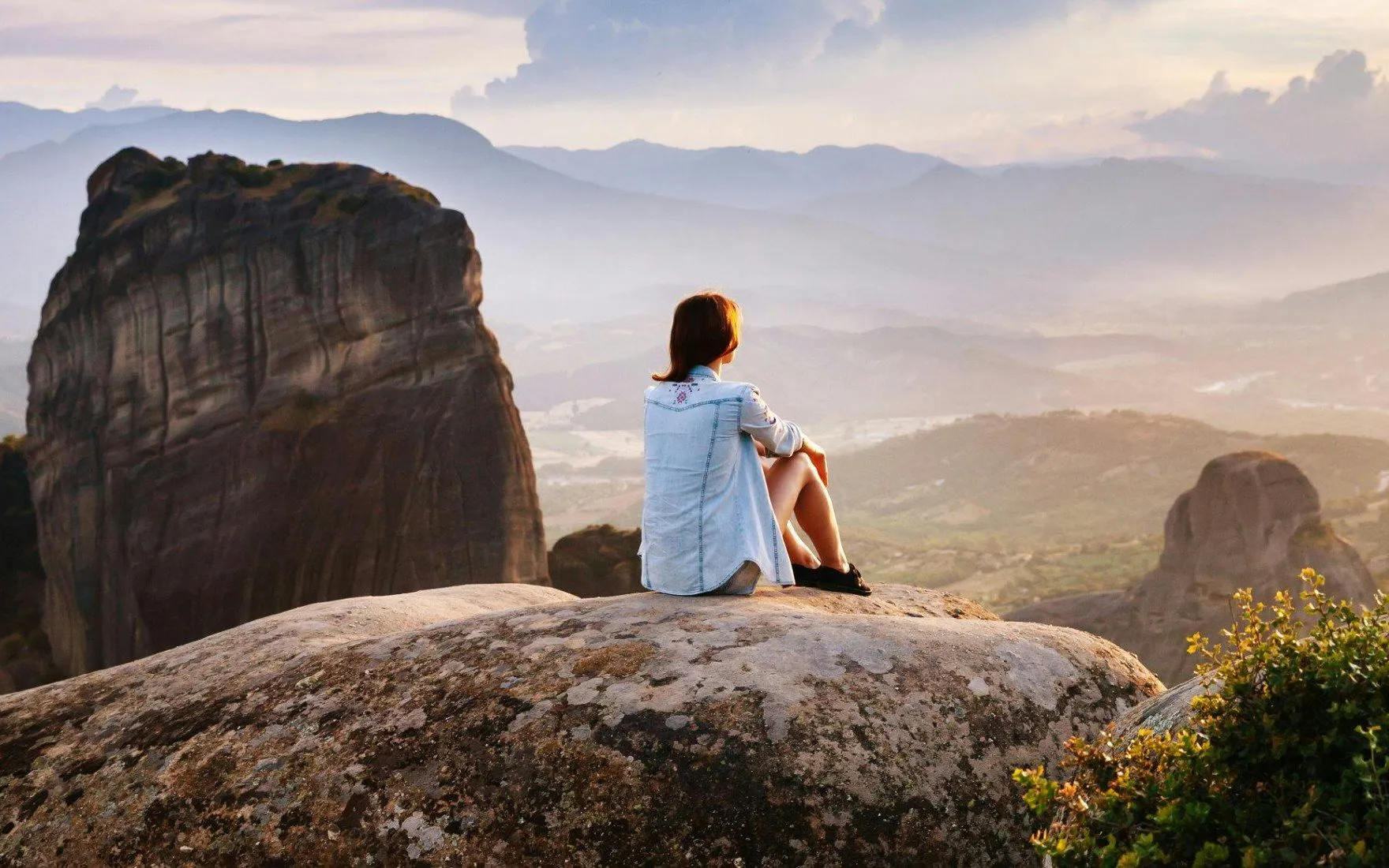 Person sitting on rock overlooking Meteora Mountains during Athens day trip.
