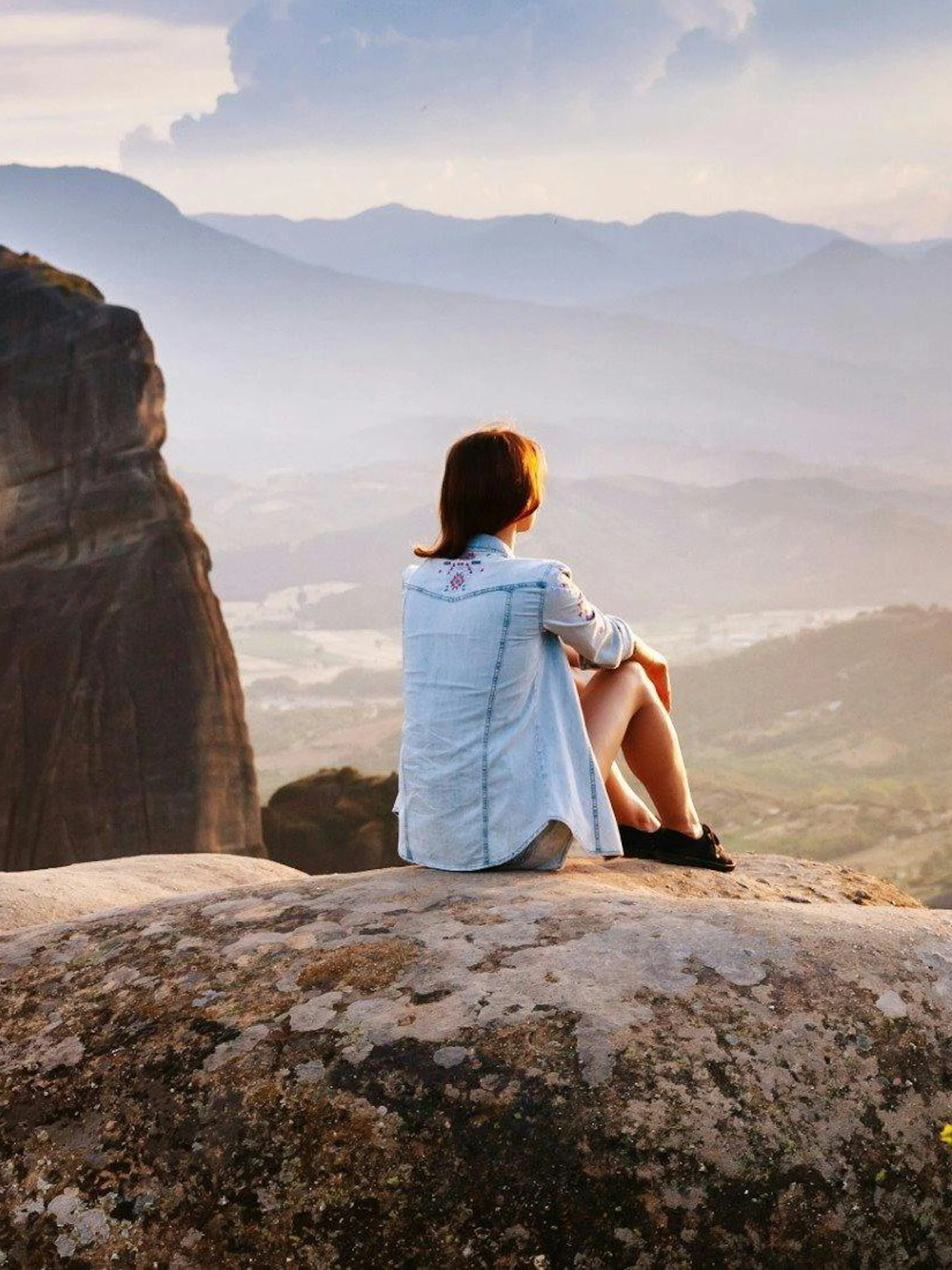 Person sitting on rock overlooking Meteora Mountains during Athens day trip.