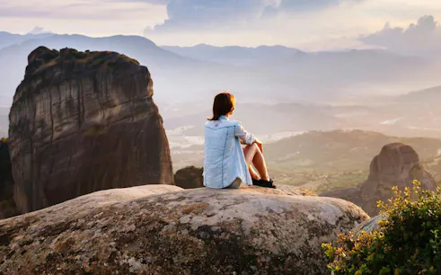 Person sitting on rock overlooking Meteora Mountains during Athens day trip.