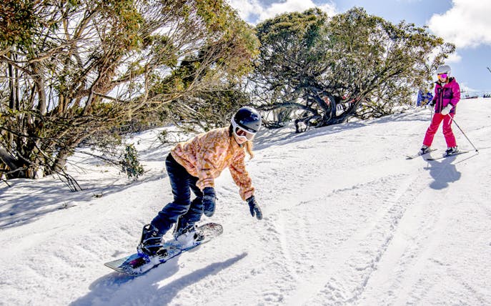 Snowboarder and skier on a snowy slope at Mt Buller, Australia.