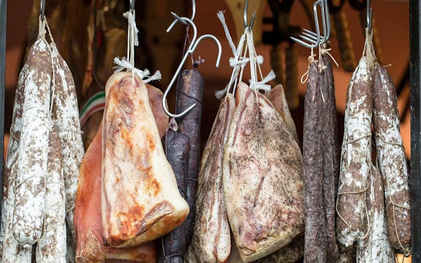Hanging cured meats at a Tuscan market for cooking class lunch.