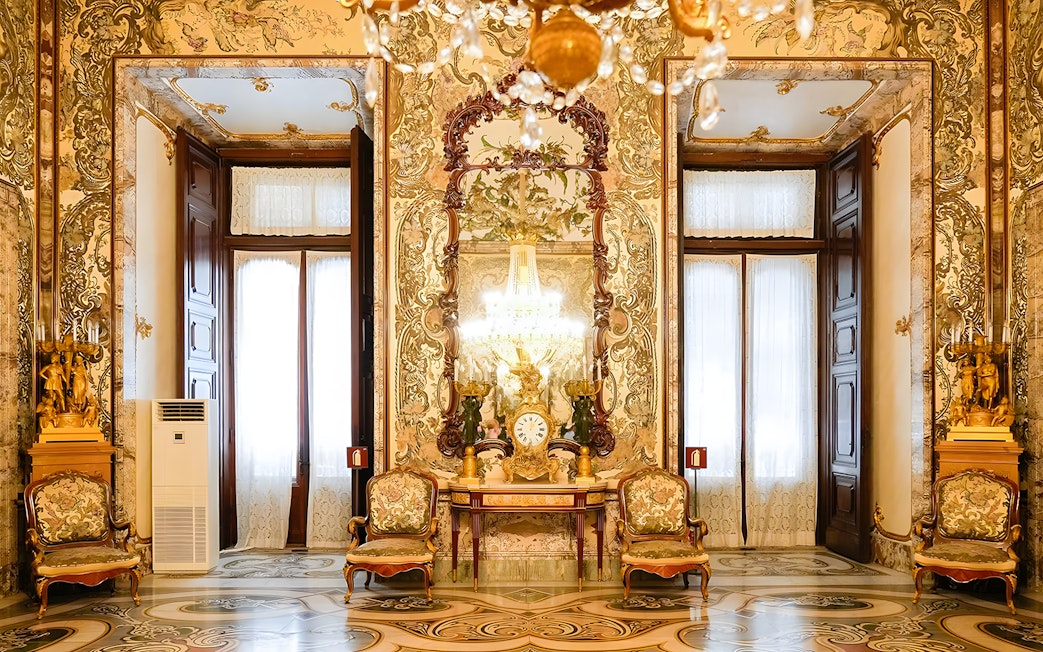 Interior of Royal Palace of Madrid with ornate decor, chandeliers, and antique furniture.
