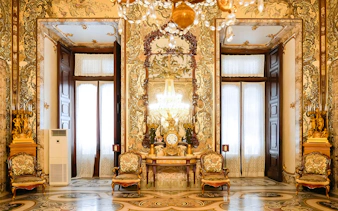 Interior of Royal Palace of Madrid with ornate decor, chandeliers, and antique furniture.