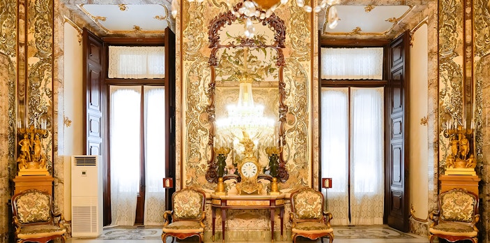 Interior of Royal Palace of Madrid with ornate decor, chandeliers, and antique furniture.