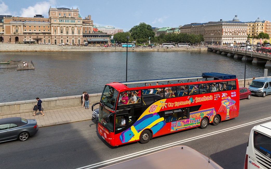 Open-top sightseeing bus near Stockholm waterfront and historic buildings.