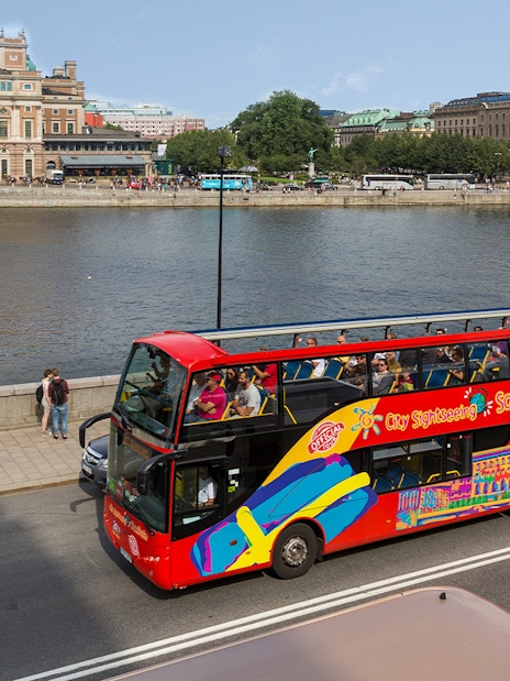 Open-top sightseeing bus near Stockholm waterfront and historic buildings.