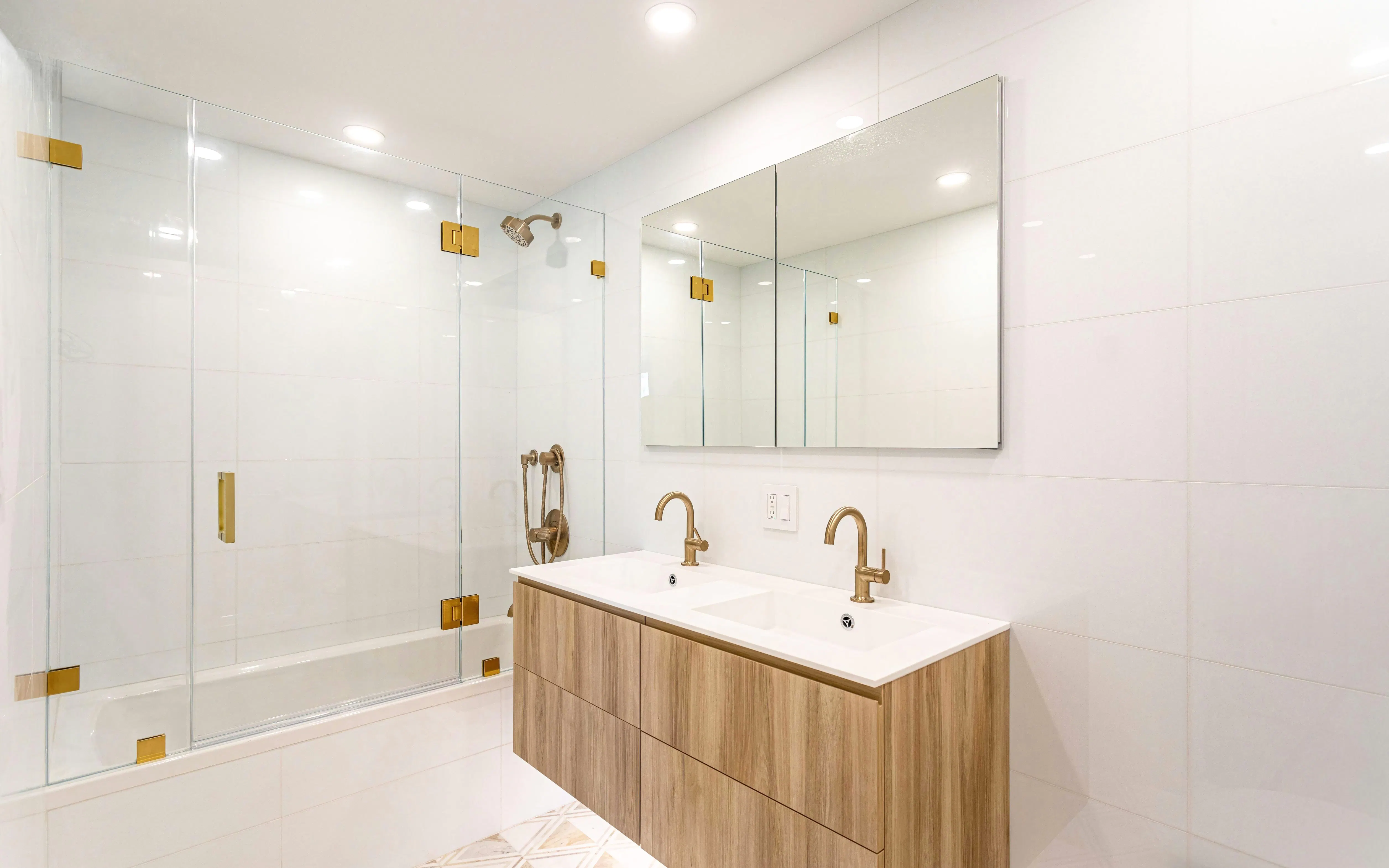 Modern white bathroom with double vanity, glass shower, and brass fixtures.