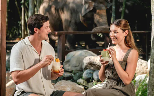 Couple enjoying drinks with elephants in the background at Elephant Explorer Bali.