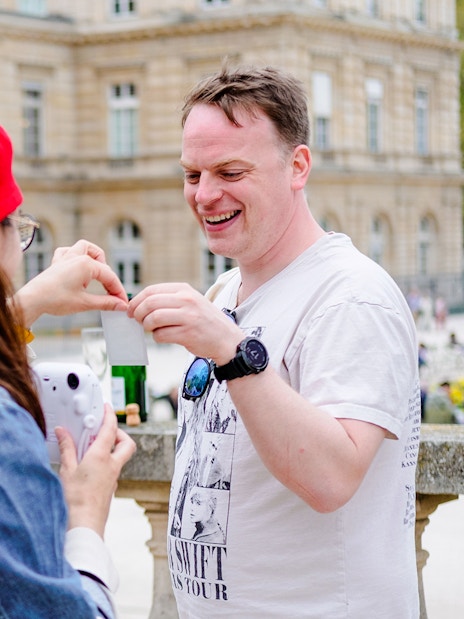 People examining a polaroid during Emily in Paris Food Tour near a historic building.