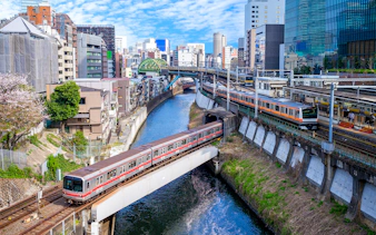 Train crossing a bridge over a river in Tokyo, Japan, with cityscape in the background.