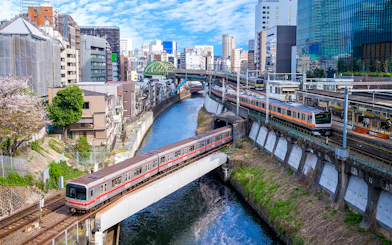 Train crossing a bridge over a river in Tokyo, Japan, with cityscape in the background.