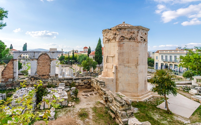 Tower of Winds in Roman Agora, Athens, with ancient ruins and cityscape in the background.