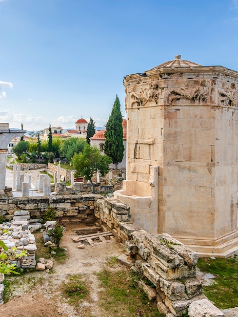 Tower of Winds in Roman Agora, Athens, with ancient ruins and cityscape in the background.