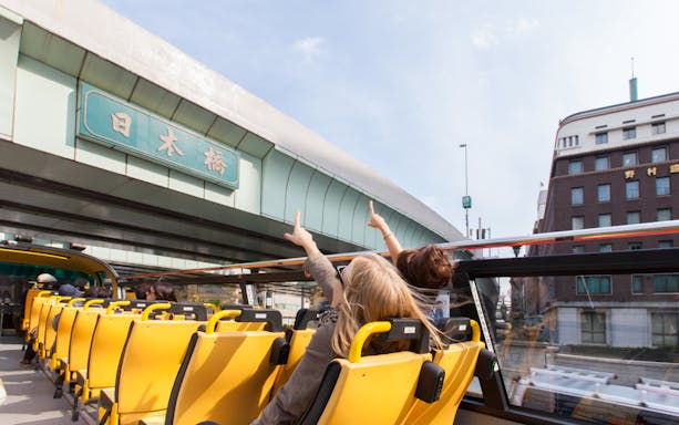 Tourists on Sky Hop bus pointing at Nihonbashi bridge in Tokyo.