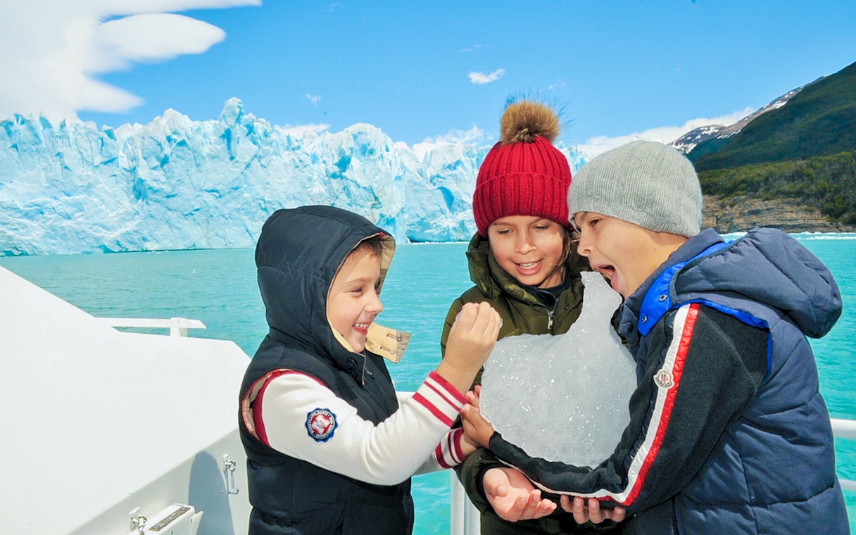 Kids enjoying ice on Perito Moreno Cruise, Argentina, with glacier in background.