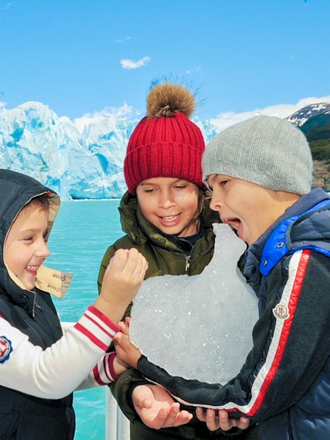 Kids enjoying ice on Perito Moreno Cruise, Argentina, with glacier in background.