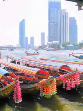 Colorful long-tail boats on Bangkok Yai Canal with city skyline in the background.