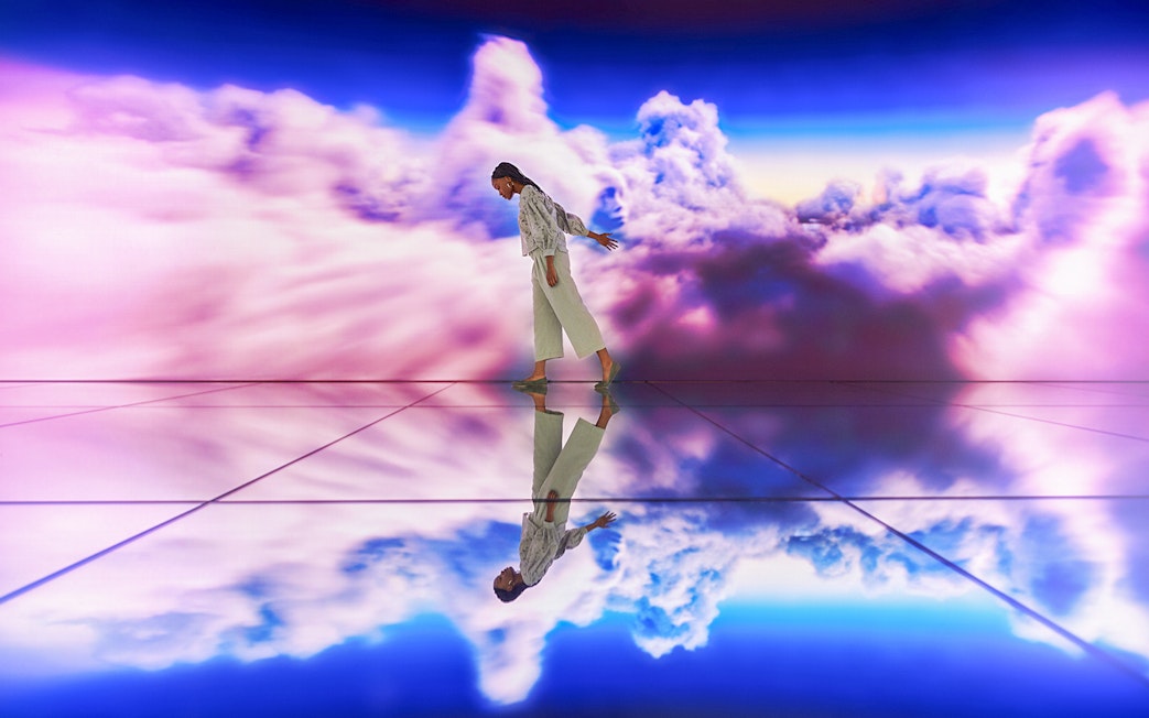 Person walking on reflective floor with vibrant cloud backdrop.